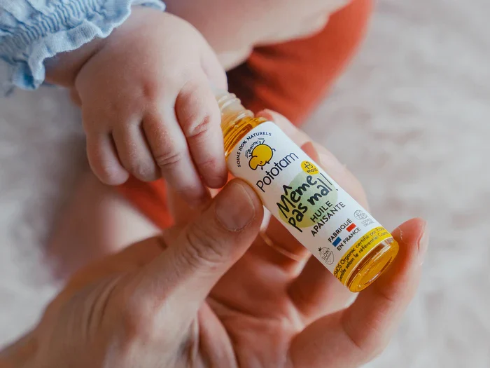 Main dans une main adulte tenant un flacon de sirop pour bébé, avec un petit doigt qui touche.
