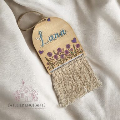 Panneau en bois avec le nom "Lana" et des fleurs colorées, orné de franges.